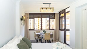 Habitación de hotel con cama, una mesa de comedor con sillas, una ventana con cortinas y vistas a edificios.