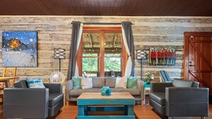 Un salon chaleureux avec un mur en bois, un canapé, deux fauteuils, une table basse et une grande fenêtre avec des rideaux.