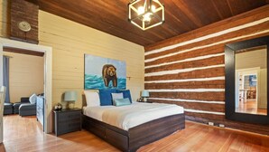 Une chambre avec un plafond en bois, un grand lit avec des oreillers bleus, une table de chevet avec une lampe et un tableau représentant un ours accroché au mur.