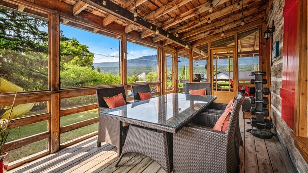 Un espace extérieur abrité, doté d'une table en verre et de chaises en osier, offrant une vue sur un paysage pittoresque.