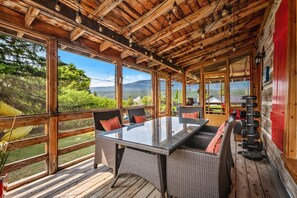 A covered outdoor area with a glass table and wicker chairs, overlooking a scenic landscape. - The Barracks | Hot Tub | Walk to Beach | Historic (Windermere)
