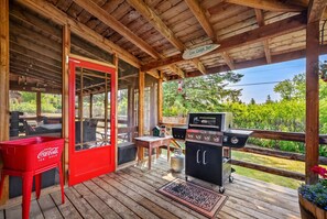 A covered outdoor area with a red Coca-Cola cooler, a barbecue grill, and a wooden deck. - The Barracks | Hot Tub | Walk to Beach | Historic (Windermere)
