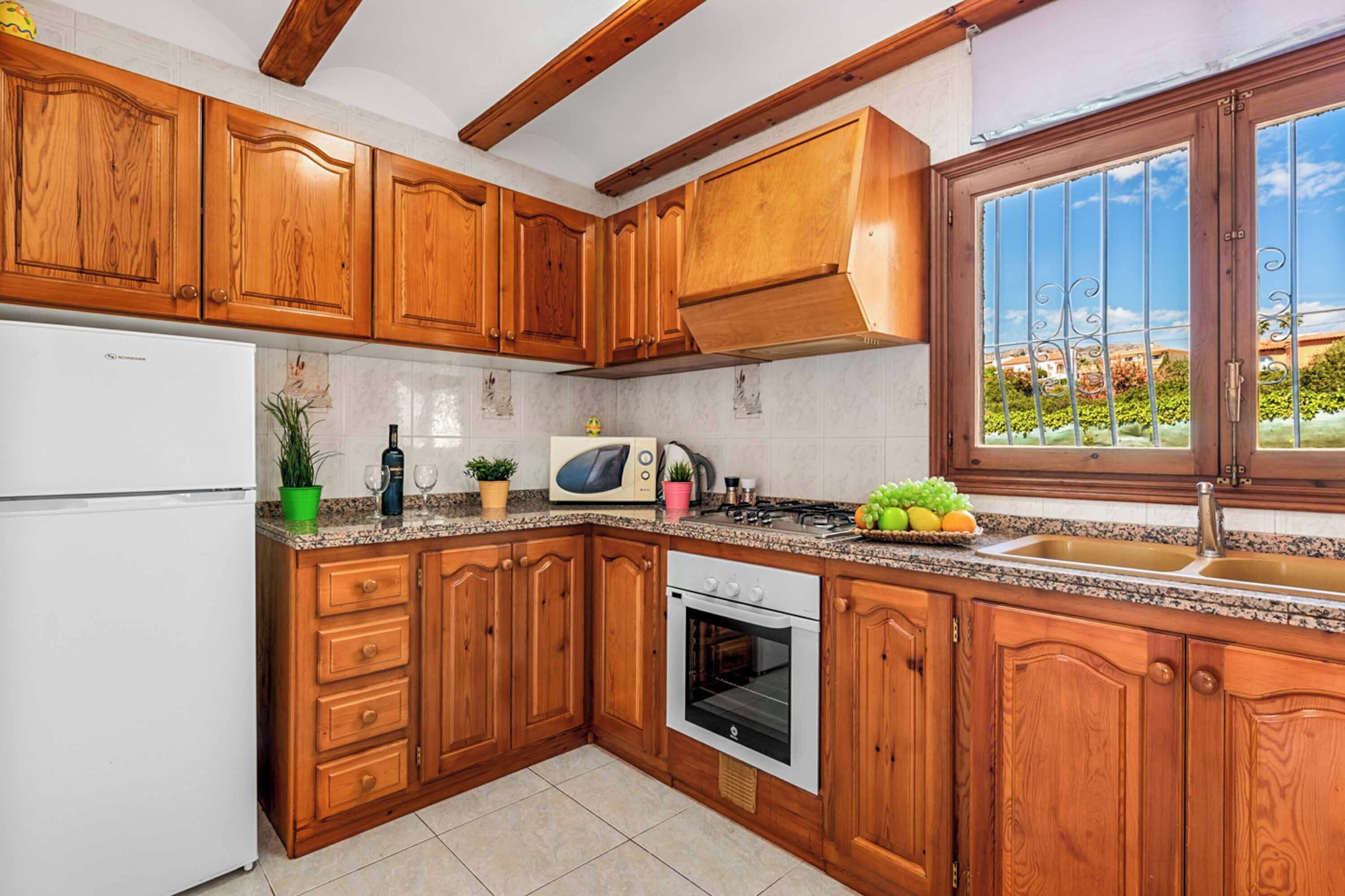 Eine Küche mit Holzausstattung, einem weißen Kühlschrank, einer Mikrowelle, einem Backofen und einem Fenster mit Blick auf Grünflächen.