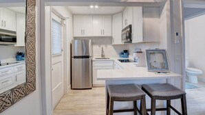 A modern kitchen with white cabinets, a stainless steel refrigerator, and a central island with stools. - Beach Bungalow  (Delray Beach)
