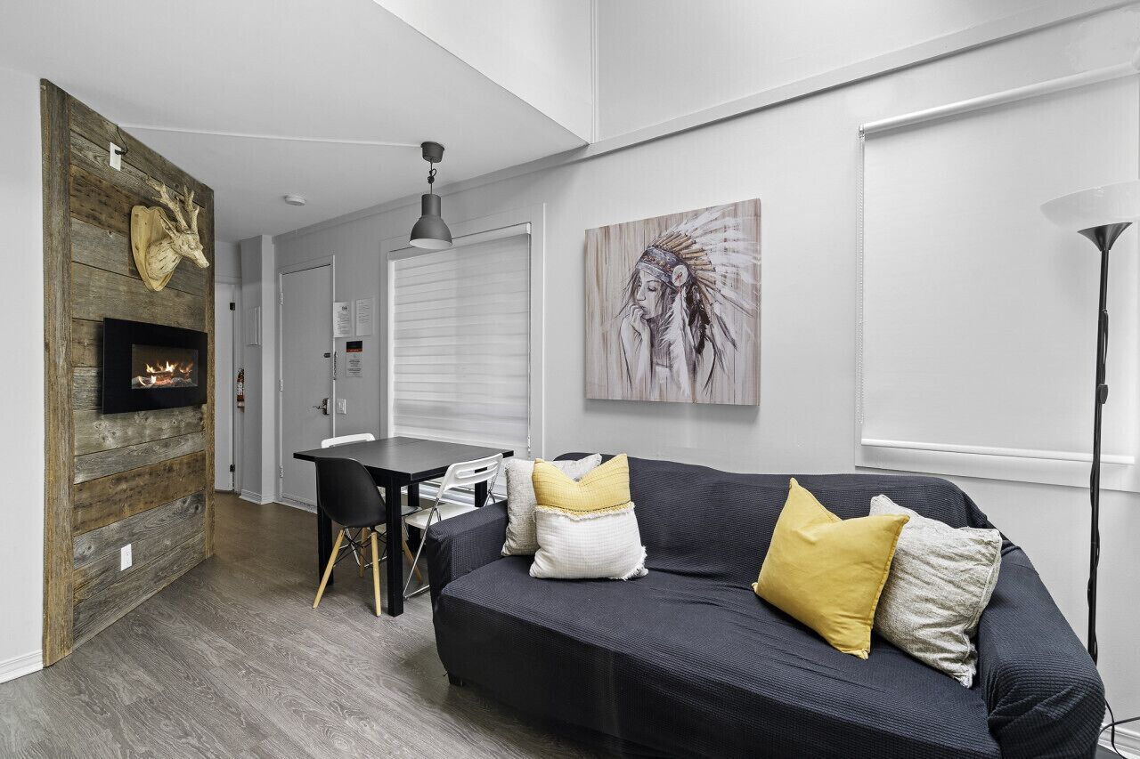 En moderne stue med pejs, en sort sofa med gule puder, et spisebord og et stort vindue.