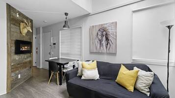 En moderne stue med pejs, en sort sofa med gule puder, et spisebord og et stort vindue.