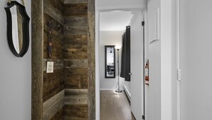 A hallway with wooden paneling on one side and white walls on the other. There is a mirror, a framed picture, and a lamp. - The Riverbed by Suite Spot (Mont-Tremblant)