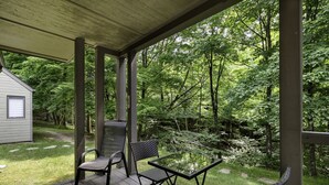 A covered patio with a table and chairs, surrounded by lush greenery and a small cabin. - The Riverbed by Suite Spot (Mont-Tremblant)