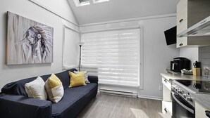 A modern kitchen with a built-in oven and a dining area with a dark-colored sofa and yellow cushions. - The Riverbed by Suite Spot (Mont-Tremblant)