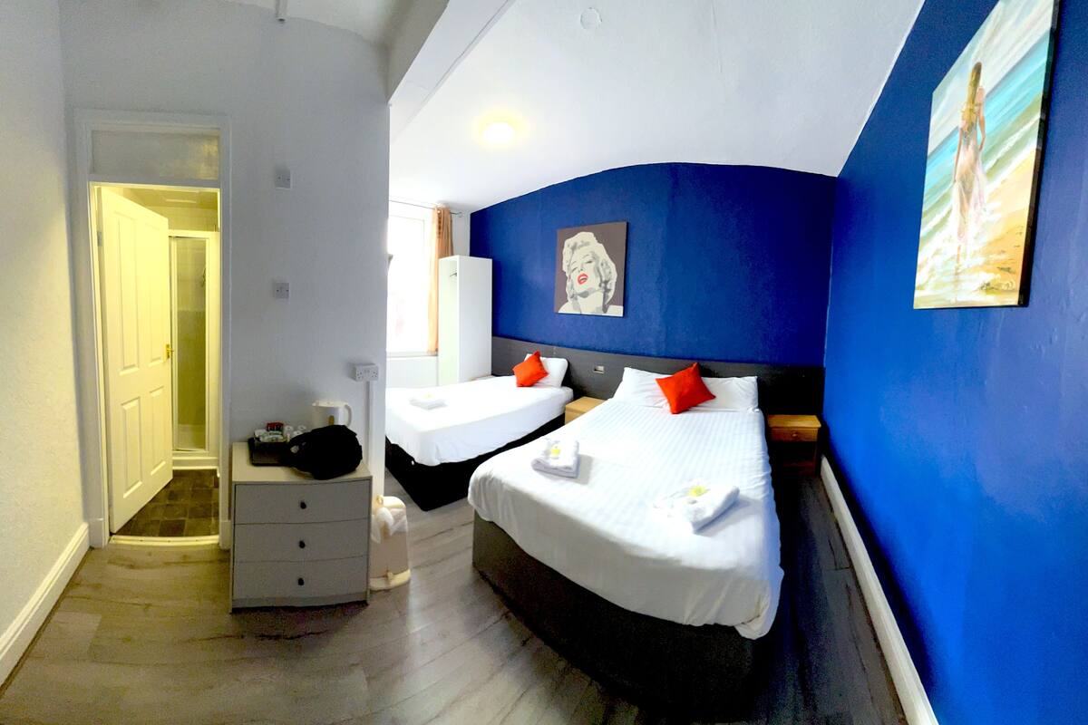 A hotel room with two beds, a dresser, a shower, and a painting on the wall.