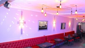 A restaurant with red upholstered booths, tables with red stools, and pendant lighting. - Calypso Hotel Blackpool (Blackpool)