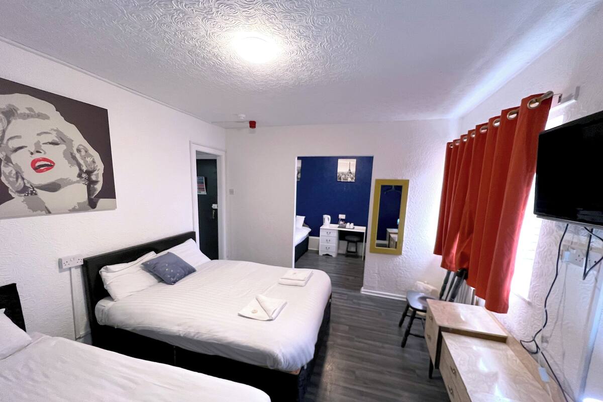 A hotel room with two beds, a desk, a chair, a TV, and a bathroom visible through an open door.