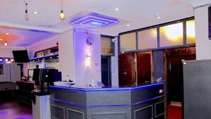 A bar area with a counter, bar stools, and a television screen. - Calypso Hotel Blackpool (Blackpool)
