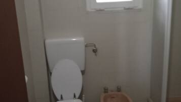 A bathroom with a toilet, bidet, and a window above the toilet.
