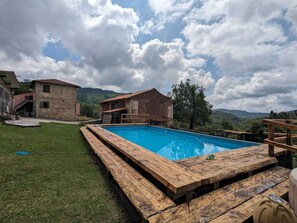 A rustic pool area with wooden deck seating, surrounded by stone buildings and a mountainous backdrop. - la debbia ranch (Rocchetta di Vara)