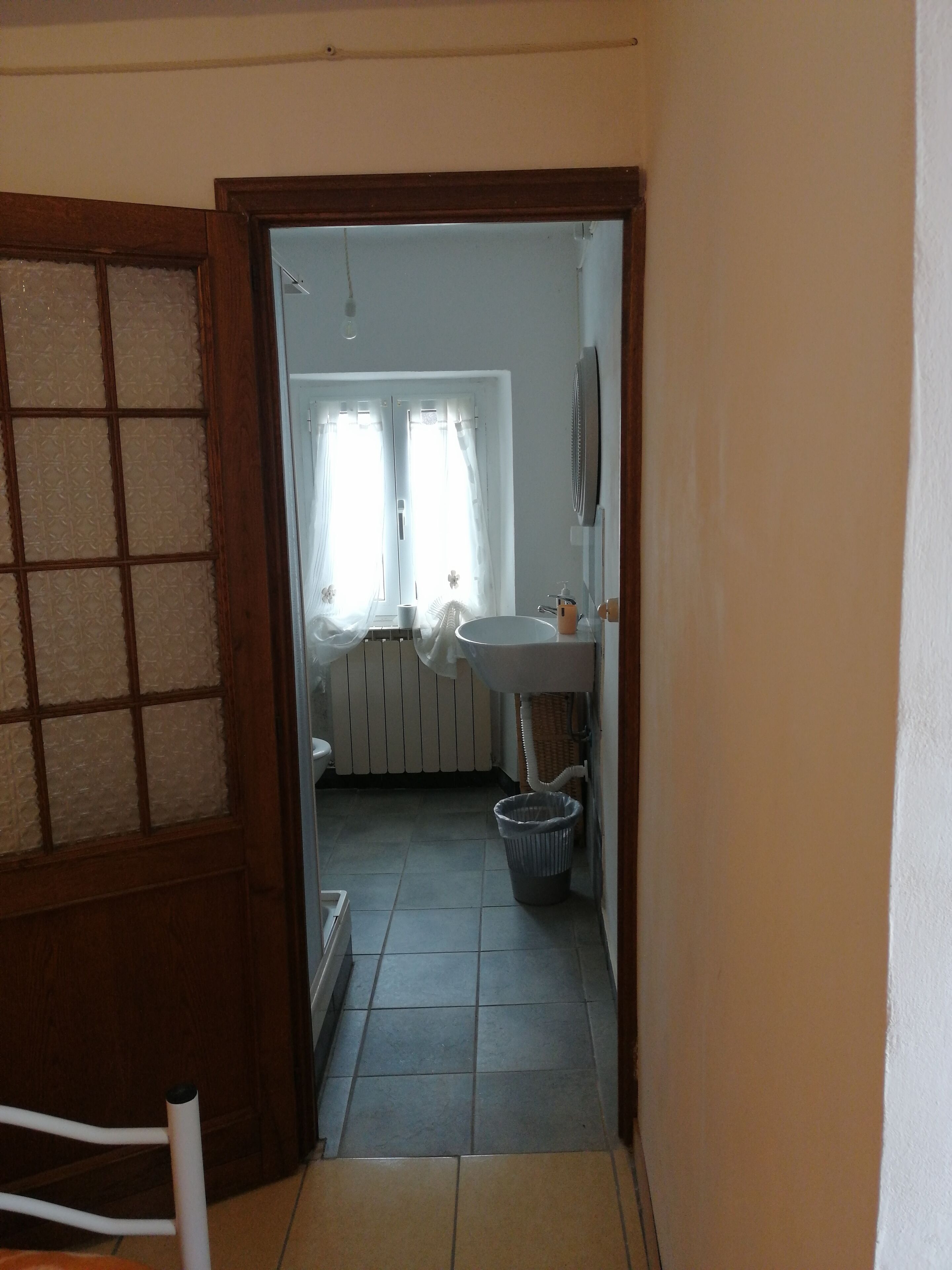 Ein schmaler Gang führt zu einem Badezimmer mit einem weißen Waschbecken, einem Heizkörper und einem Mülleimer.