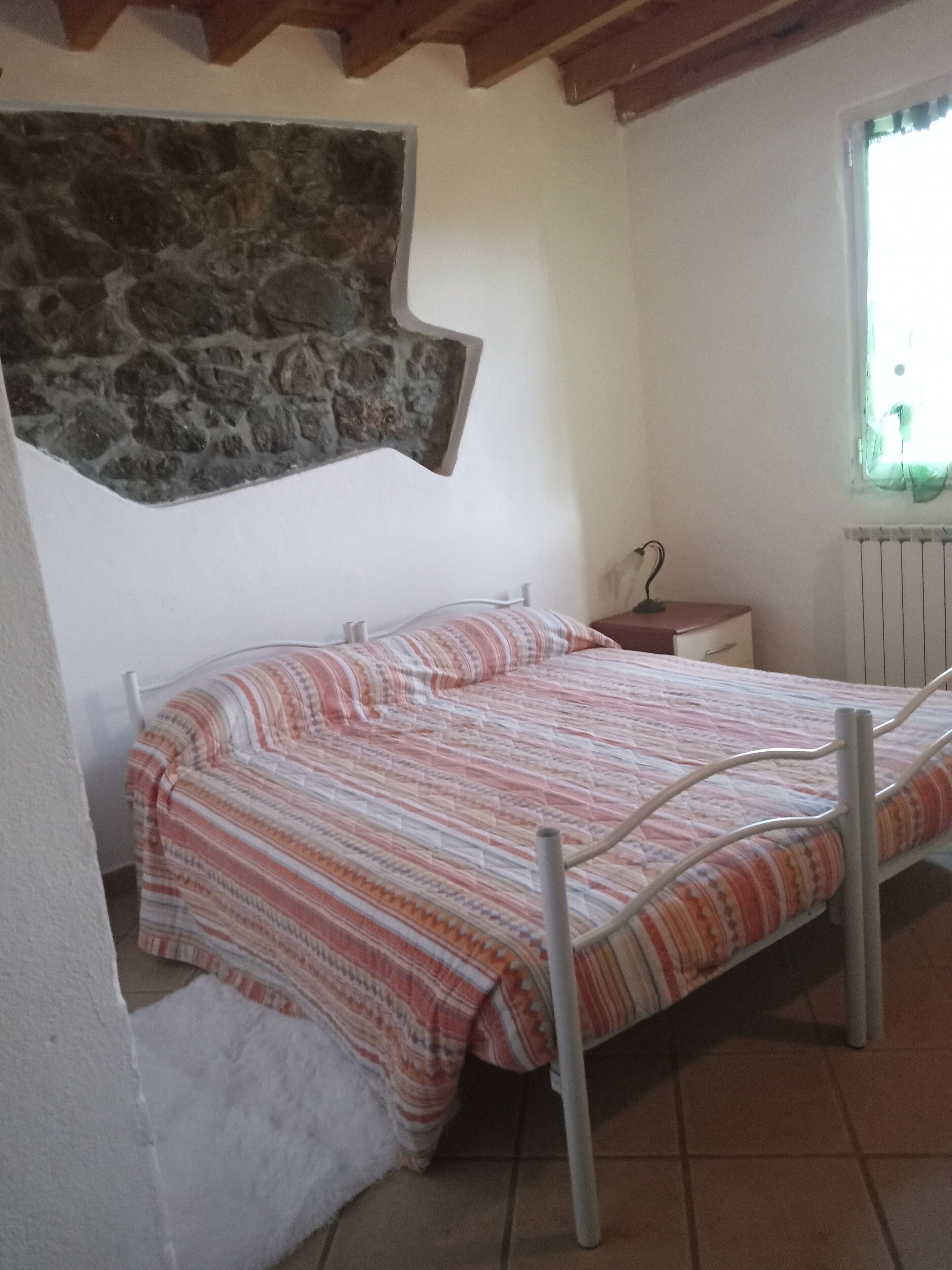 Un dormitorio pequeño y acogedor con una cama individual, una pared de piedra, un radiador y una ventana con cortinas.