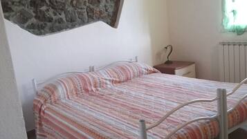 Un dormitorio pequeño y acogedor con una cama individual, una pared de piedra, un radiador y una ventana con cortinas.