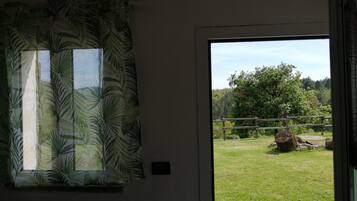 A room with a window featuring a tropical leaf pattern curtain, a view of a grassy outdoor area with a wooden fence and trees.