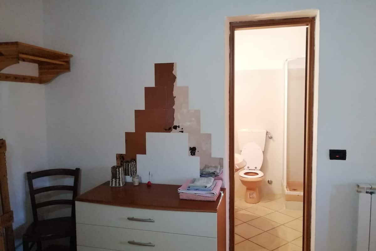 A small bathroom with a wooden vanity, a chair, and a toilet visible through an open door.