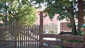 A wooden gate with a stone wall, a tree, and a building in the background. - la debbia ranch (Rocchetta di Vara)