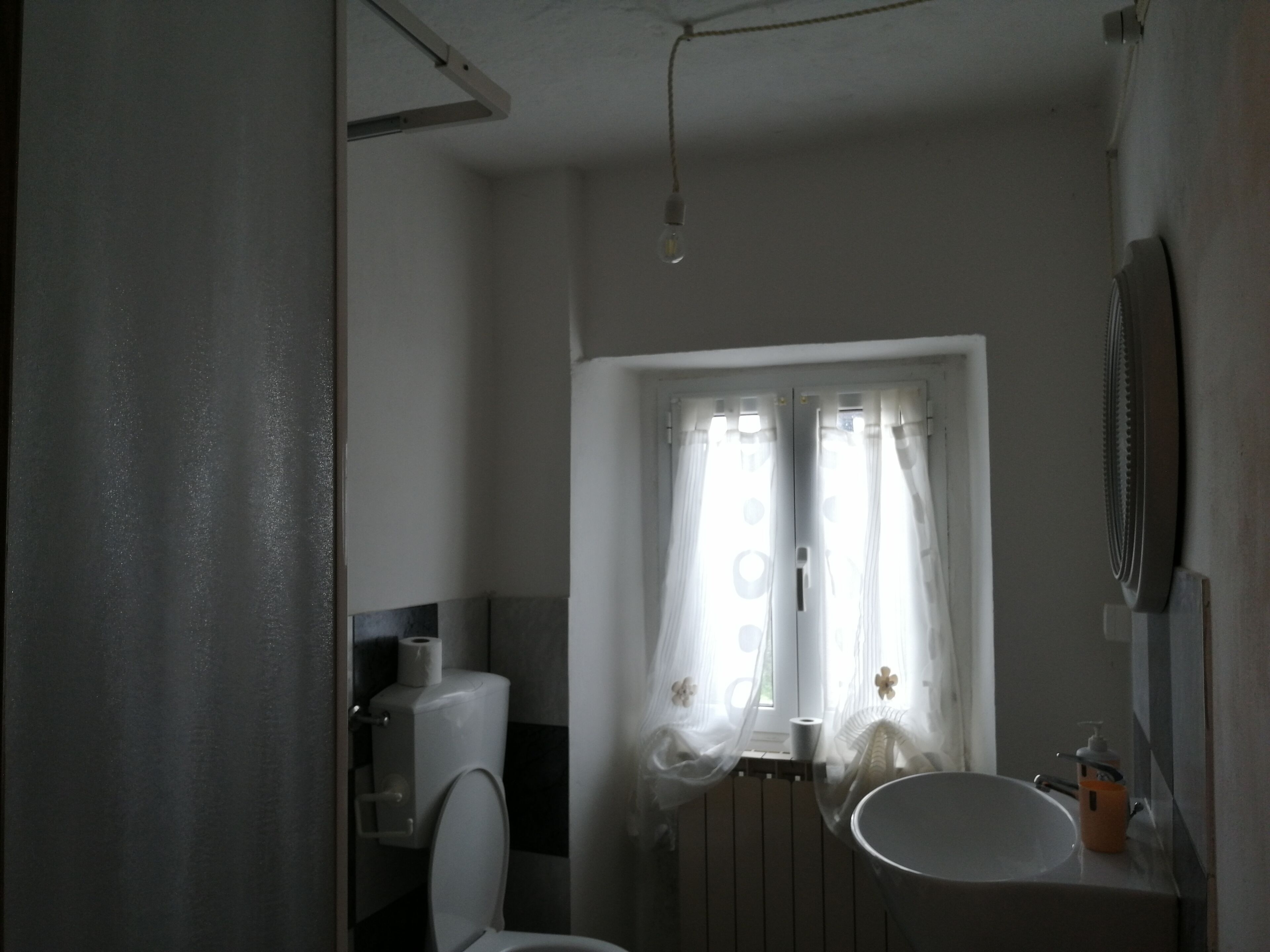 Baño con inodoro, lavabo y ventana con cortinas.