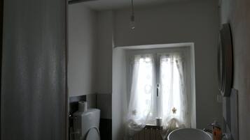Baño con inodoro, lavabo y ventana con cortinas.