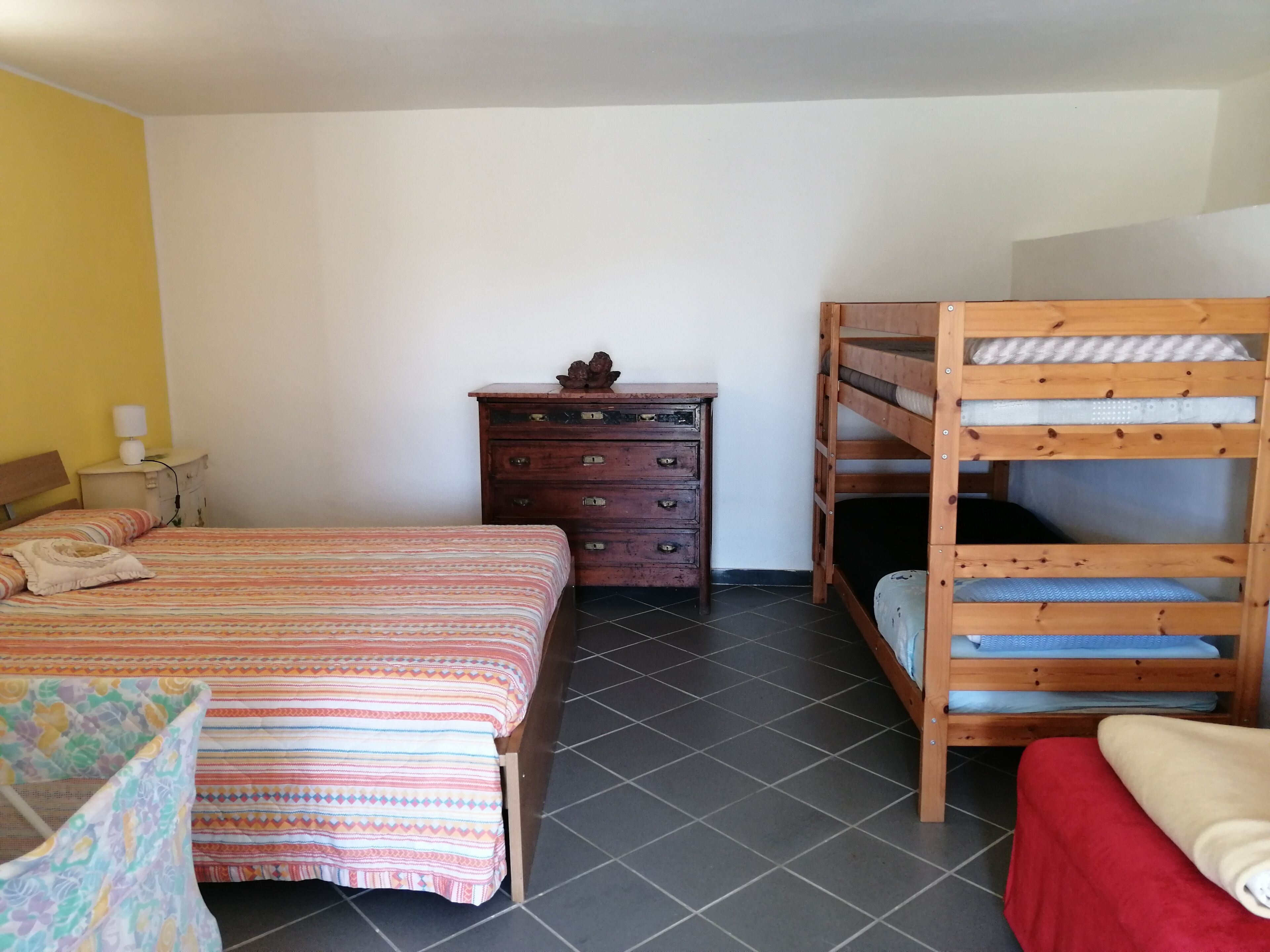 A bedroom with a bed, a dresser, a wooden bunk bed, and a nightstand with a lamp.