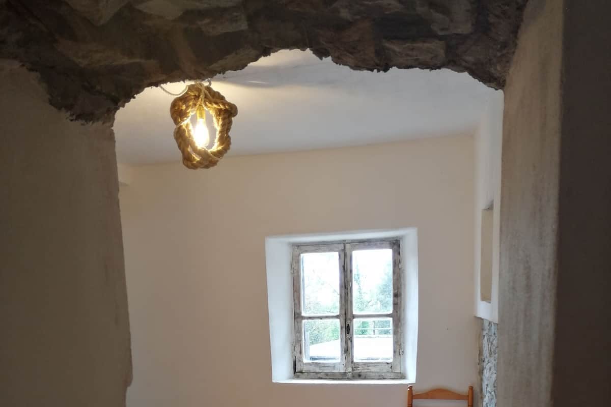 A bedroom with a bed, a window, and a hanging light fixture.