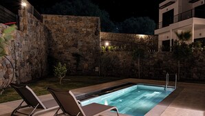 A swimming pool with two lounge chairs, stone walls, and a modern building in the background. - AL MARE (Bodrum)