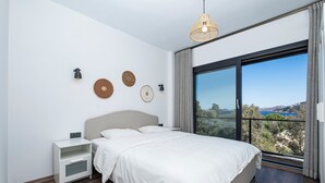 A bedroom with a large bed, a nightstand, a wall-mounted lamp, and a view of the outdoors through a large window. - AL MARE (Bodrum)