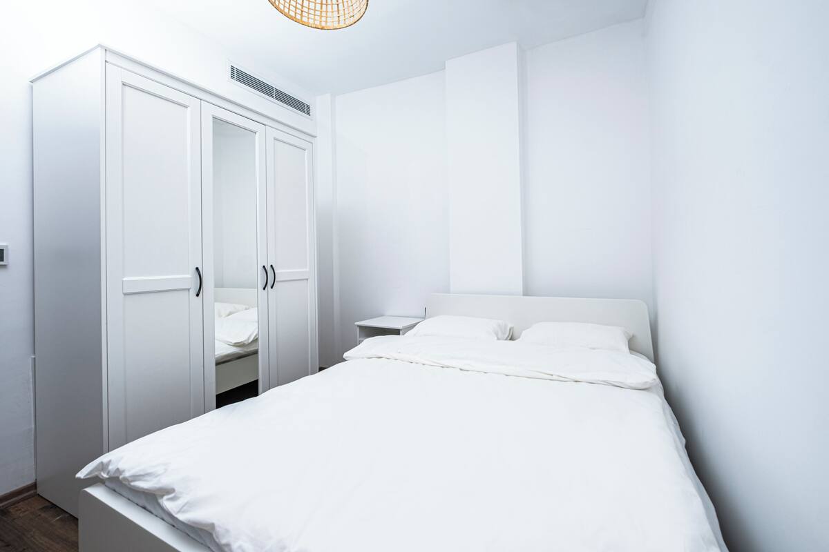 A minimalist bedroom with a bed, white wardrobe, and a nightstand.