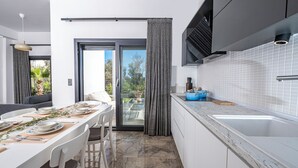 A modern kitchen with white cabinets, a blue pot on the counter, and a dining area with a table set for four. - AL MARE (Bodrum)