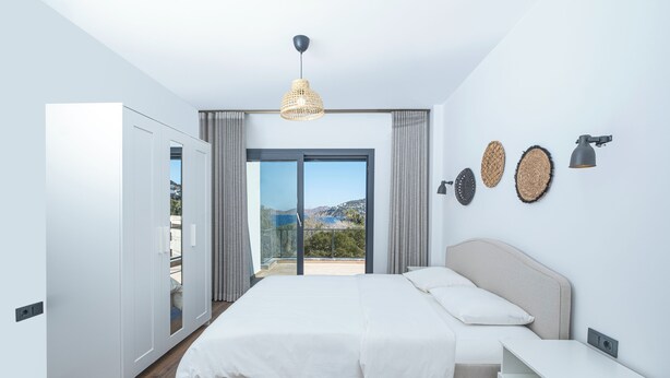 A modern bedroom with a large bed, a wardrobe, a bedside table, and a view of the outdoors. - AL MARE (Bodrum)