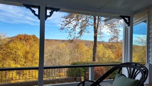 A porch with a view of autumn foliage, a chair, and a railing.