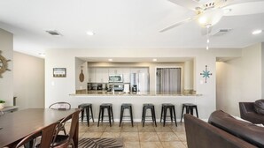 A modern kitchen with white cabinets, a central island with bar stools, and a dining area with a table and chairs. - Lakefront Escape with a View! Your Lake Conroe Vacation Starts Here (Montgomery)