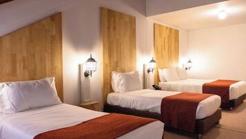 A hotel room with three beds, each with white bedding and a brown blanket. There are wall-mounted lamps on either side of the beds.