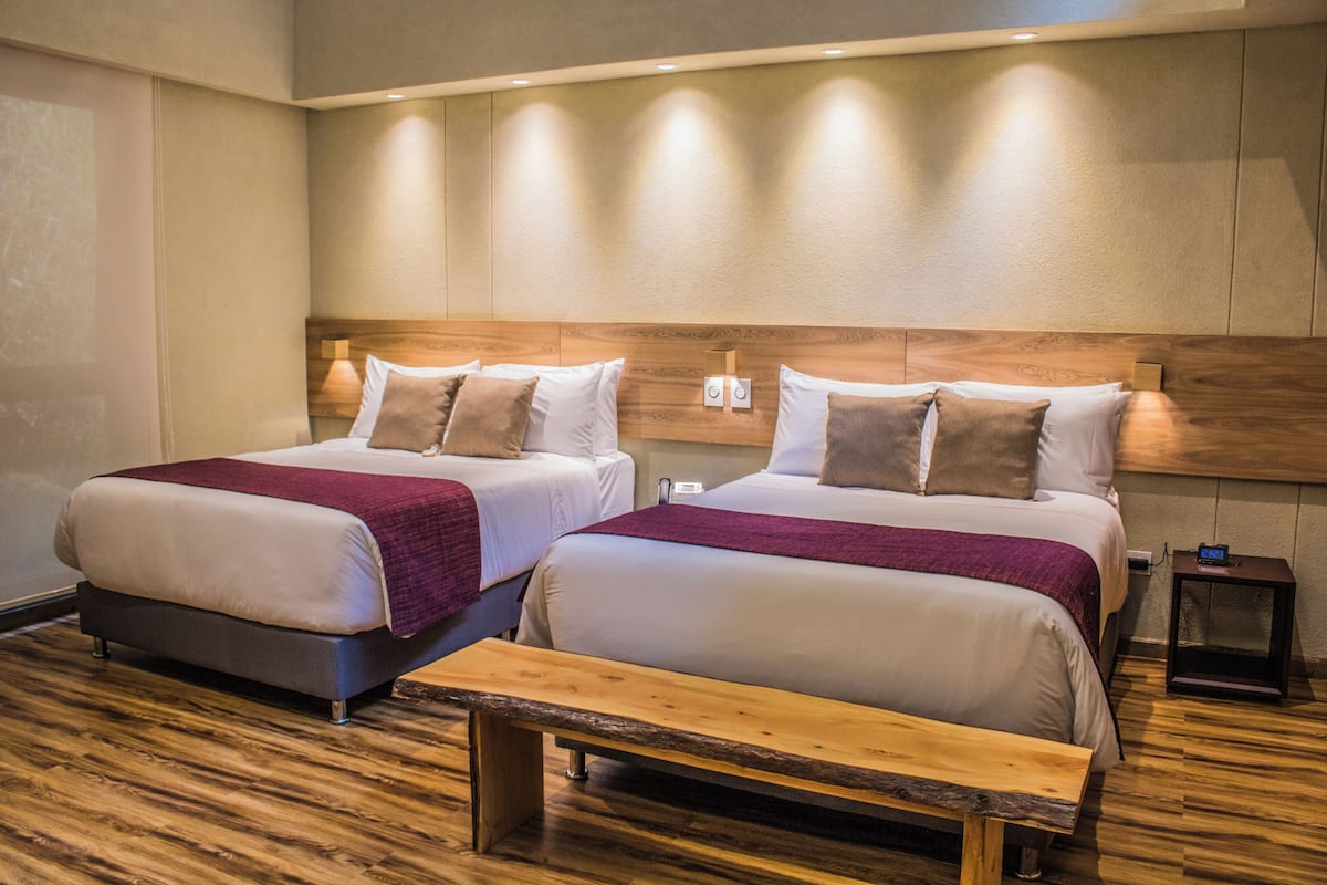 Ein Hotelzimmer mit zwei Betten, einer Holzbank und einem Nachttisch mit einer Uhr.