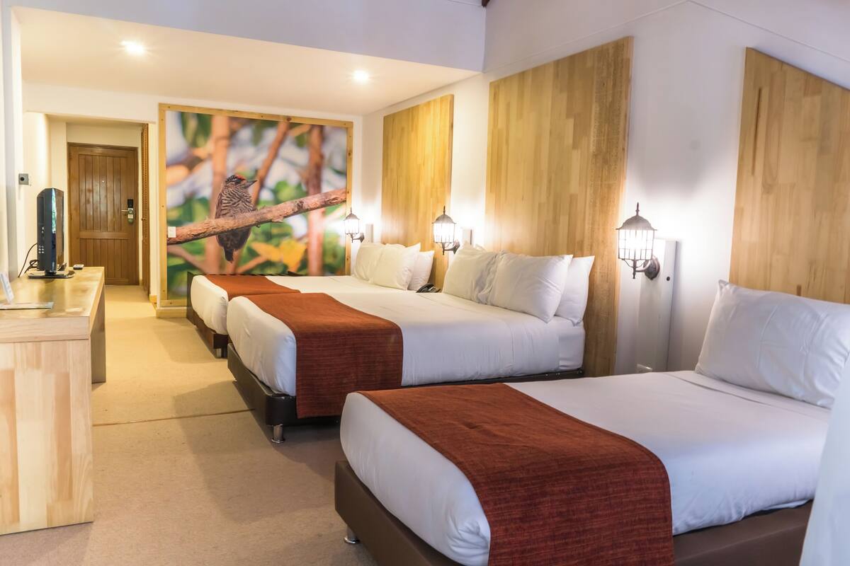 Ein Hotelzimmer mit drei Betten, Holz-Kopfteilen und einem Wandbild von einem Vogel auf einem Ast.