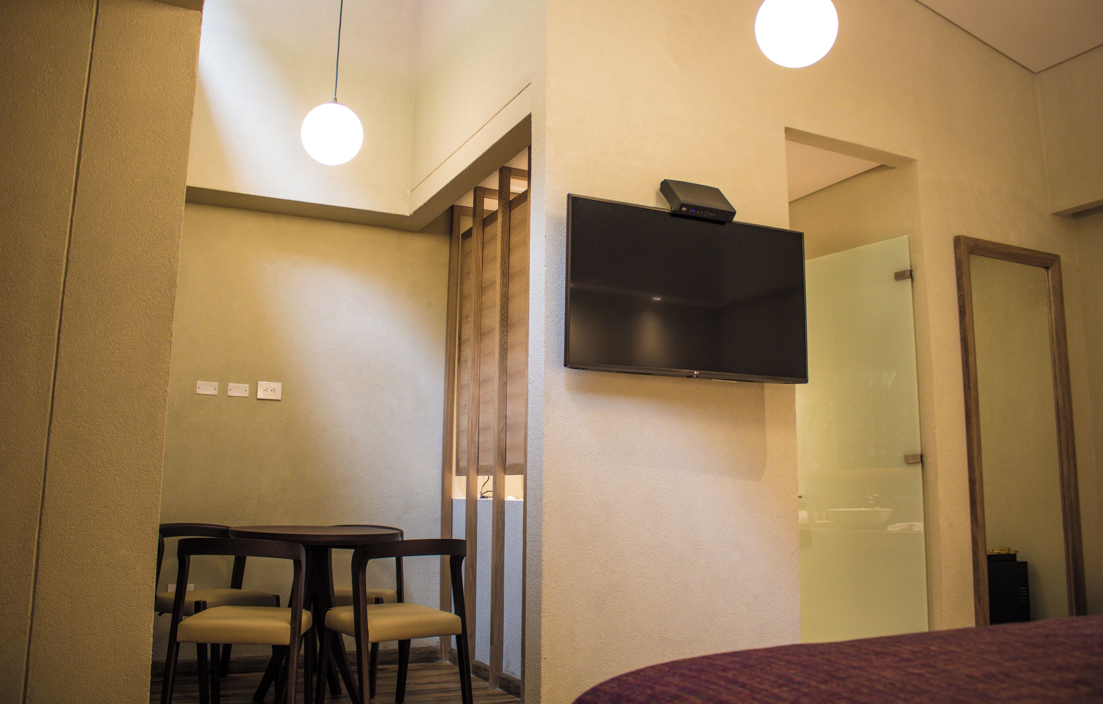 A hotel room with a flat-screen TV mounted on the wall, a small table with two chairs, and a bed with a purple blanket.