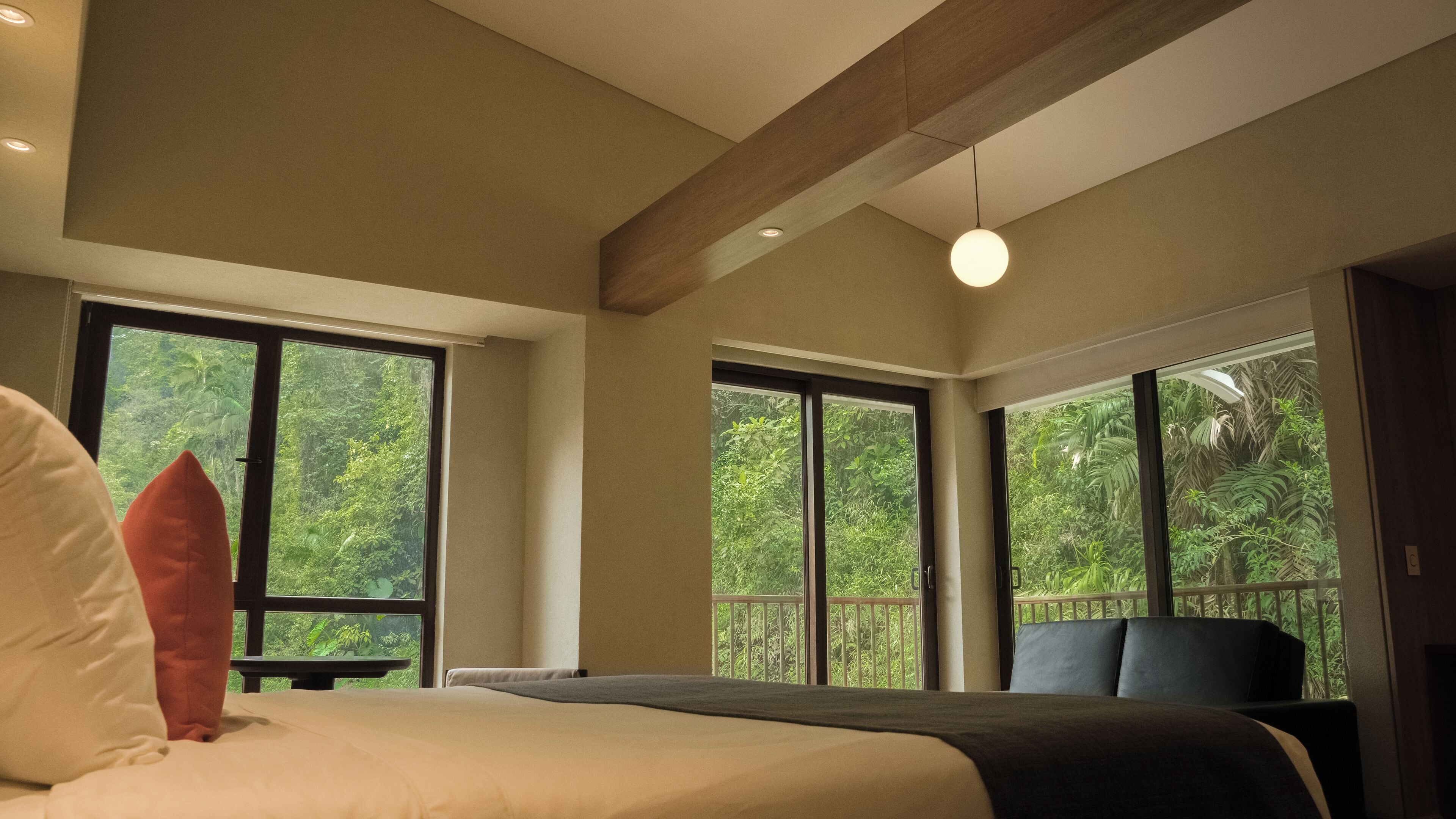 A bedroom with a large bed, a nightstand, and a window with a view of lush greenery.