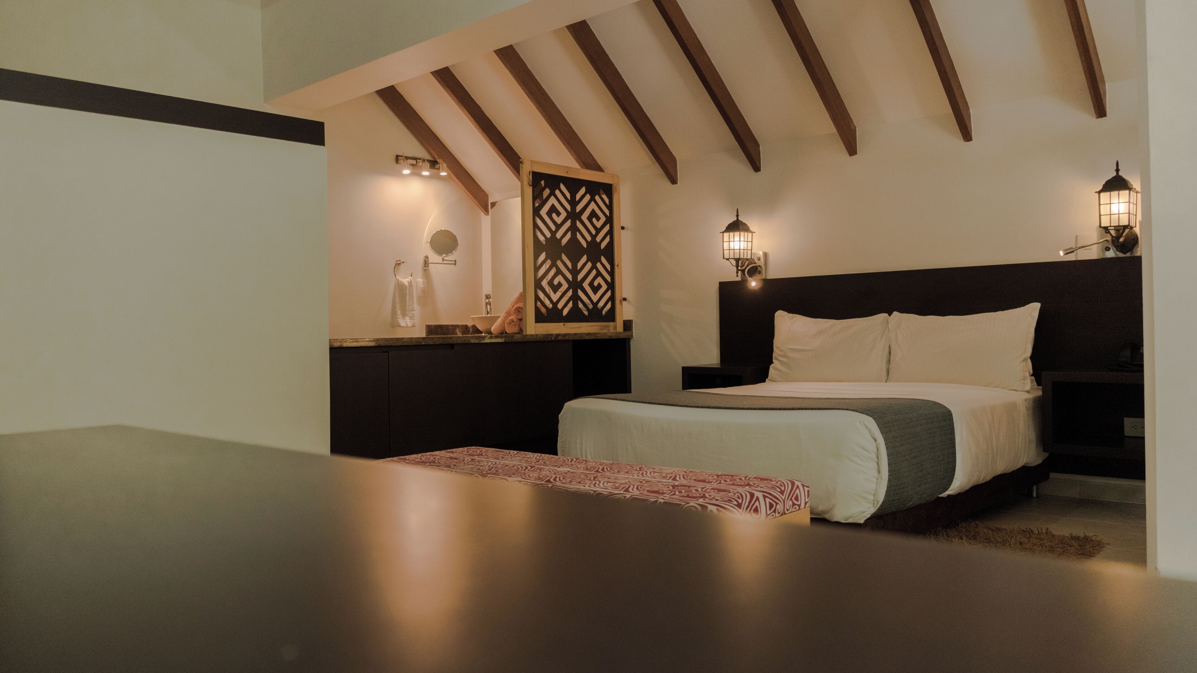 A bedroom with a bed, bedside lamps, a nightstand, a mirror, and a decorative wall panel.