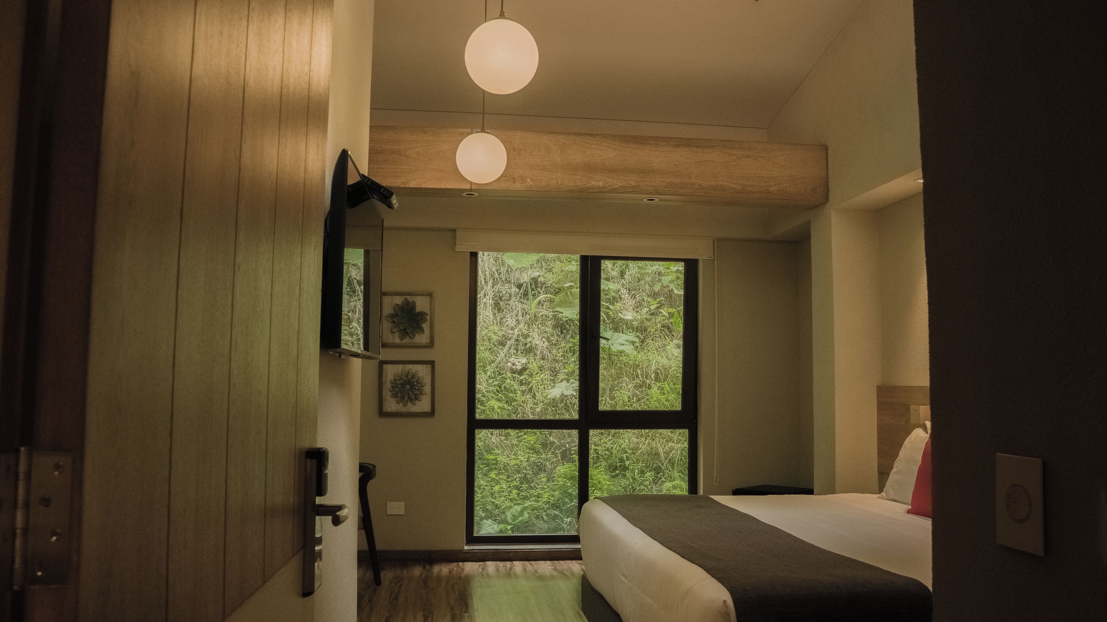 A bedroom with a large window, a bed, a bedside table, and a hanging light fixture.