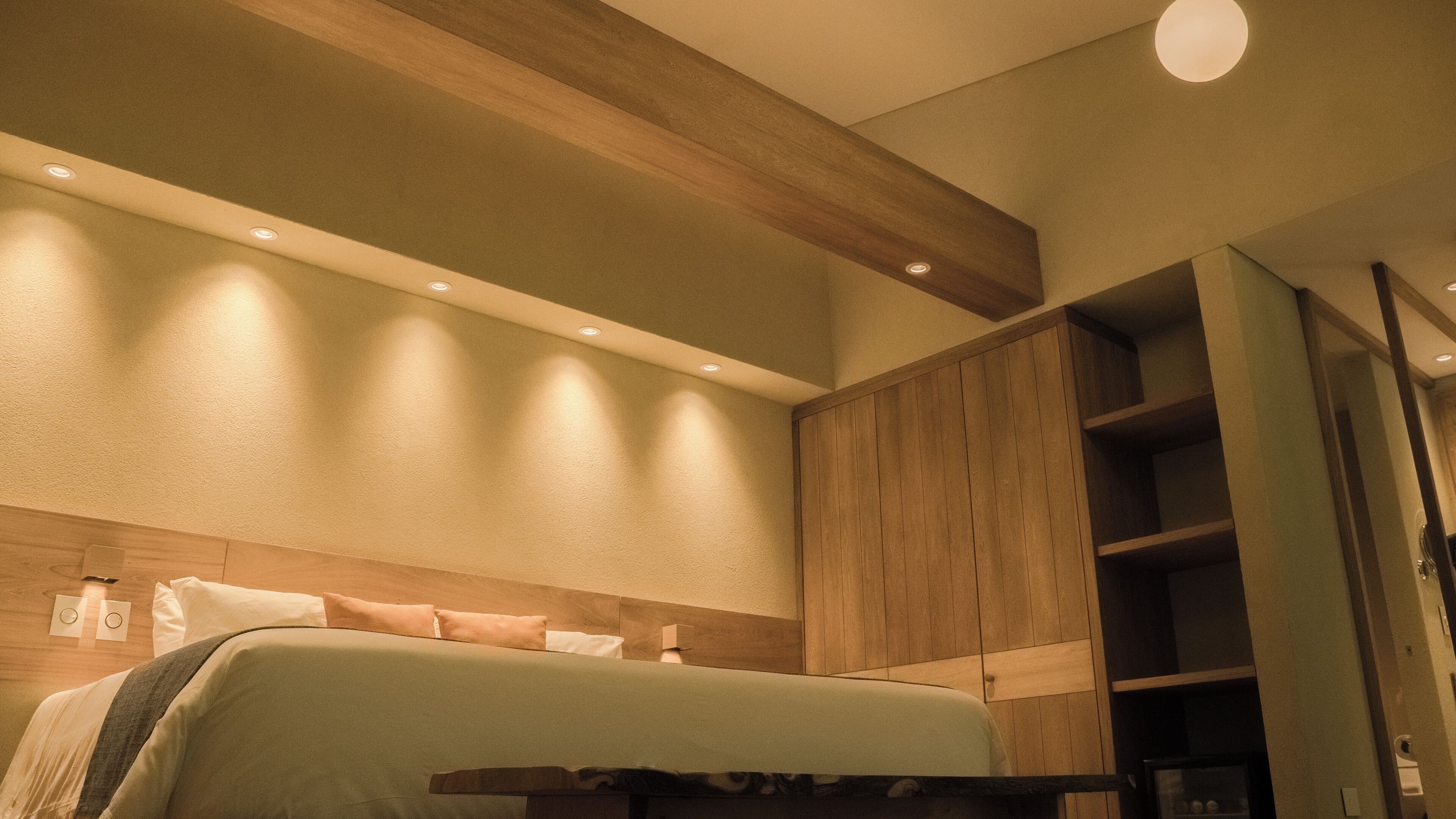 Quarto de hotel com cama, painéis de madeira, uma prateleira e uma porta.