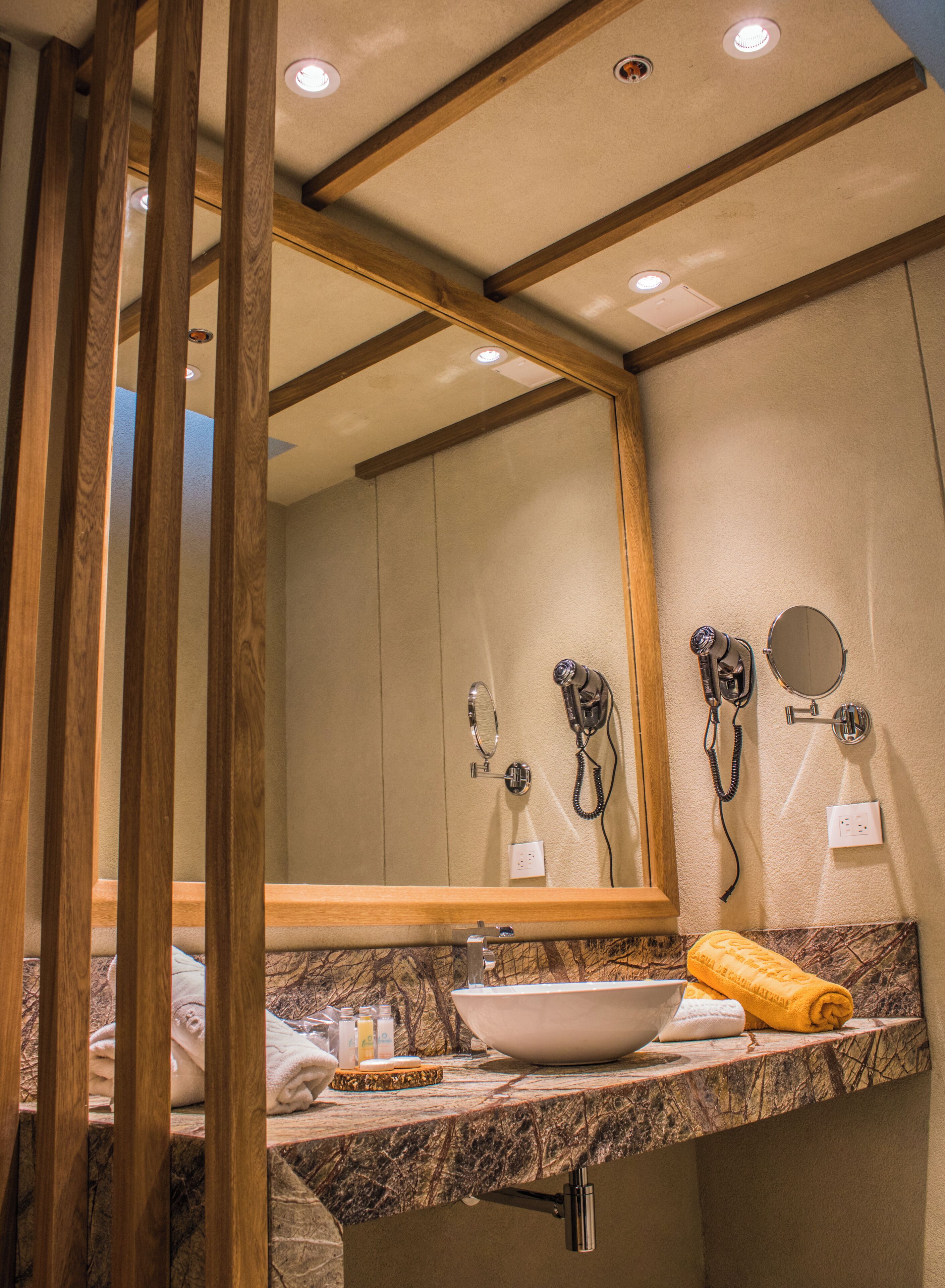 Un baño con un espejo de marco de madera, un lavabo con encimera de mármol, un secador de pelo y una toalla.