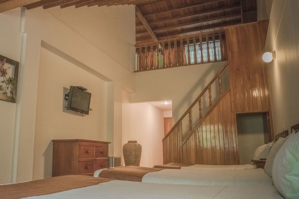 Ein Hotelzimmer mit einer Holztreppe, einem Bett, einem Schminktisch und einem an der Wand befestigten Fernseher.