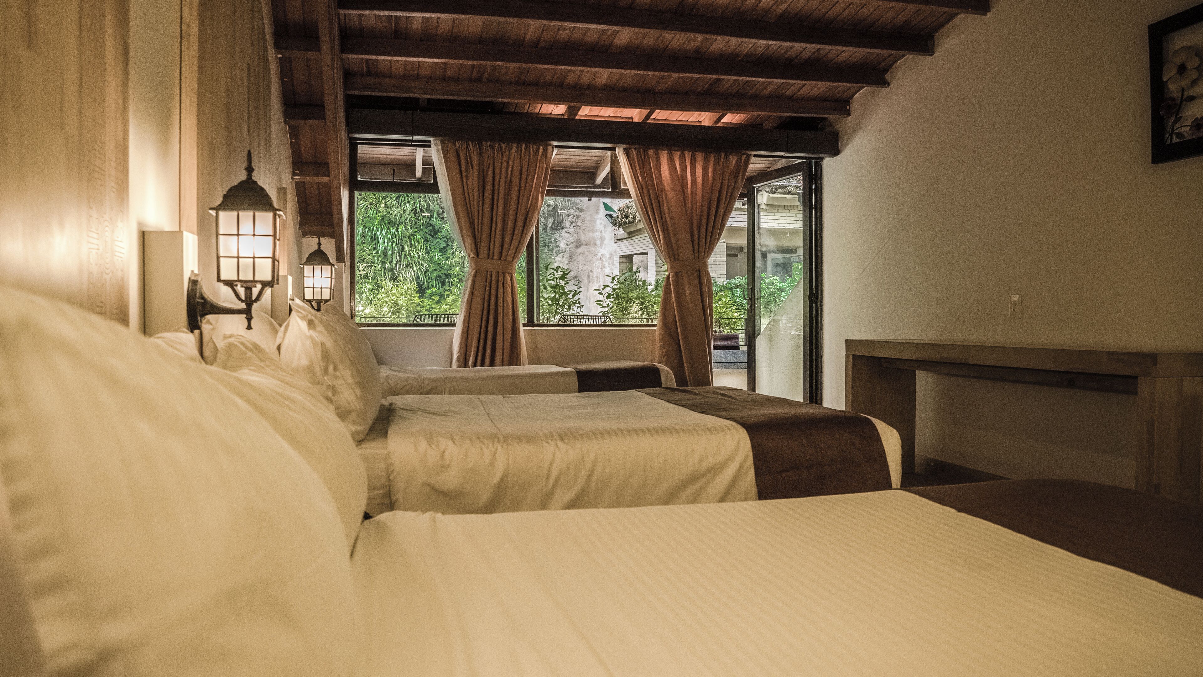 Une chambre avec deux lits, une fenêtre avec des rideaux et une vue sur la verdure.
