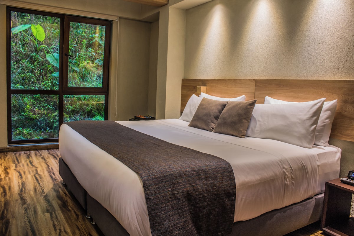 Ein Schlafzimmer mit einem großen Bett, einem Holzkopfstück und einem Fenster mit Blick auf Grünflächen.