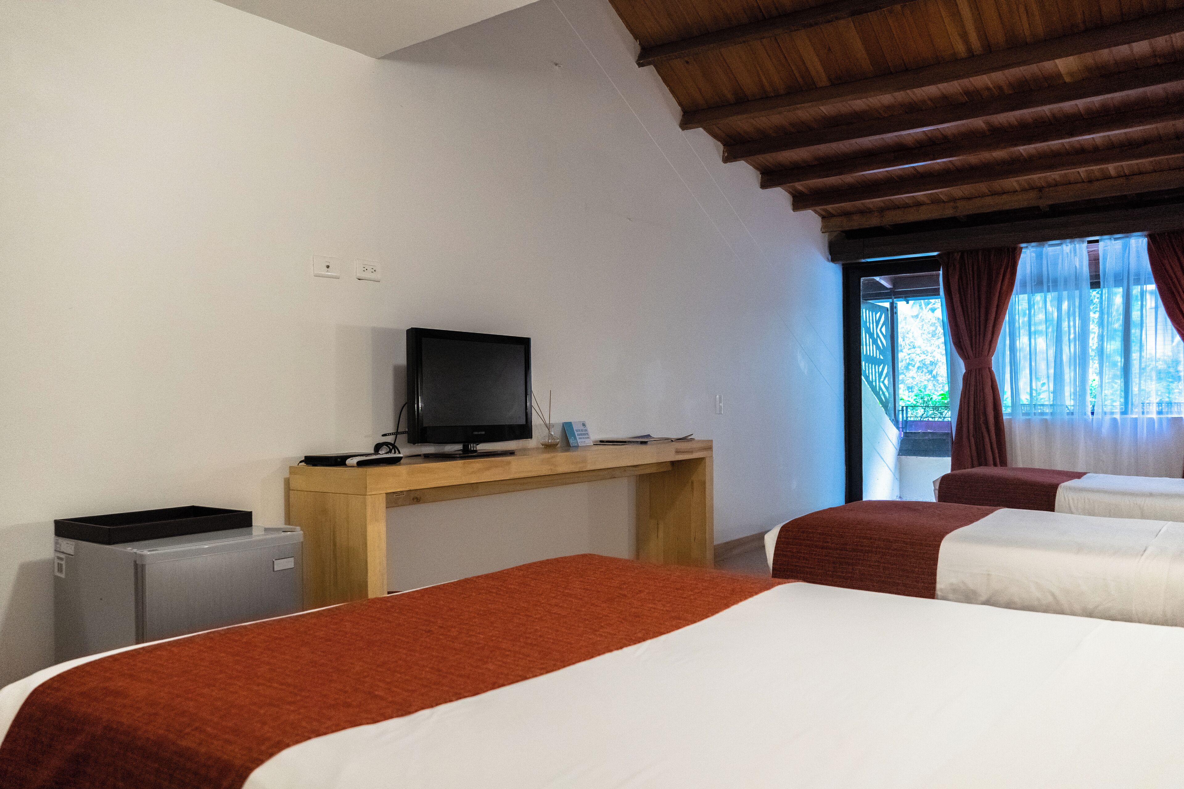A hotel room with two beds, a desk with a television, and a window with curtains.