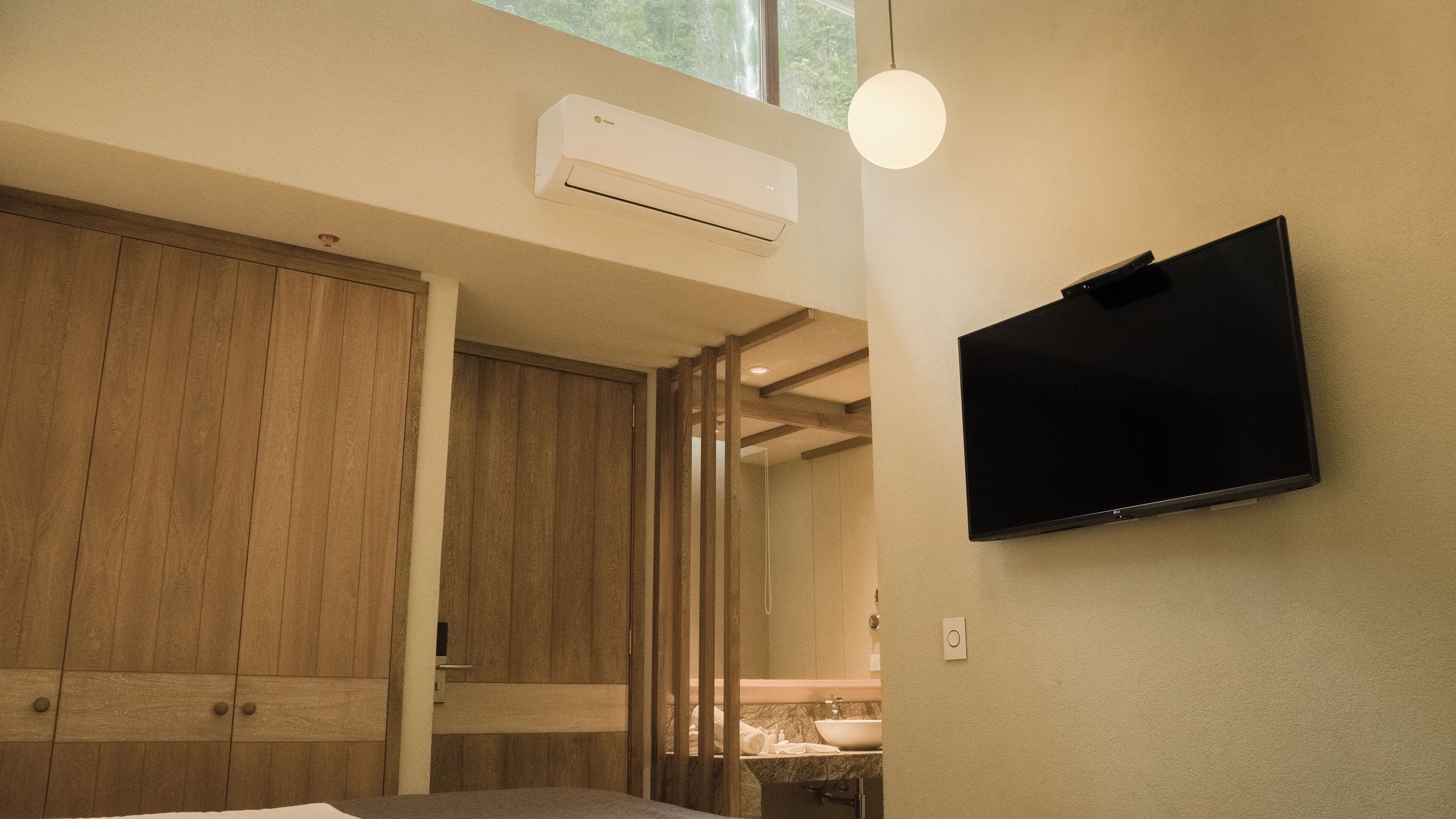 A modern bathroom with a wooden door, a mounted TV, and a ceiling-mounted air conditioner.